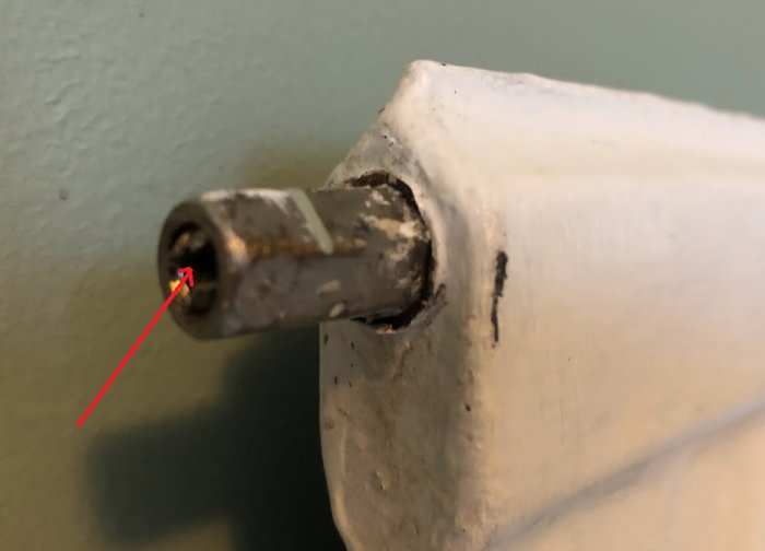 Ett vitmålat metallstång med rost och slitage som syns; röd pil pekar på detalj.