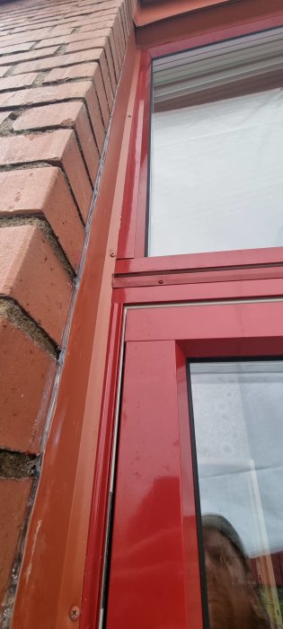 Ett rött fönsterparti mot en tegelvägg, med spegling av någons ansikte.