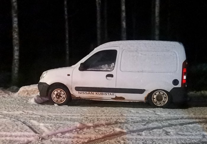 En vit Nissan Kubistar skåpbil parkerad i snö vid skogsnatt. Rear beteckningen synlig.