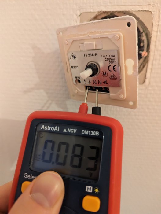 Multimeter mäter låg spänning på termostat. Vägg installation. Händer. Teknisk felsökning. Temperaturkontroll.