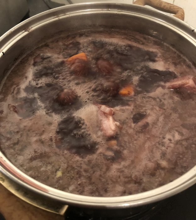 En gryta med kokande mörk vätska och matbitar på spisen.
