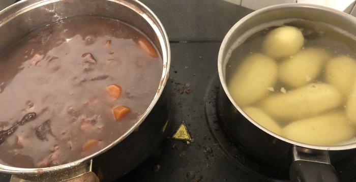 Två kastruller på spis, en med köttgryta, andra med potatis, smutsig spishäll.
