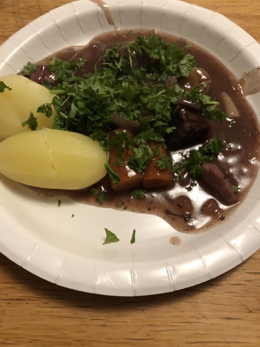 En tallrik mat med potatis, brunsås och persilja på ett vitt engångstallrik.