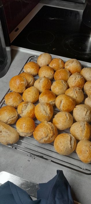 Färska, nybakade bullar på ett kylgaller, köksmiljö, bakplåt och spis i bakgrunden.