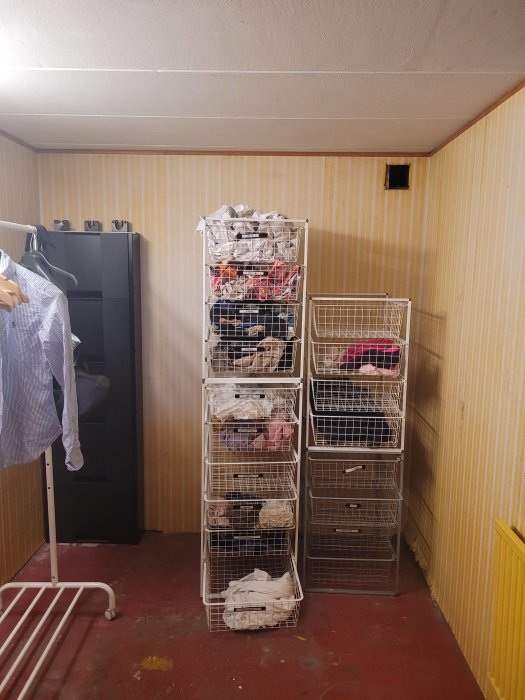 Tvättstuga med staplade trådkorgar fulla av kläder och klädhängare till vänster.
