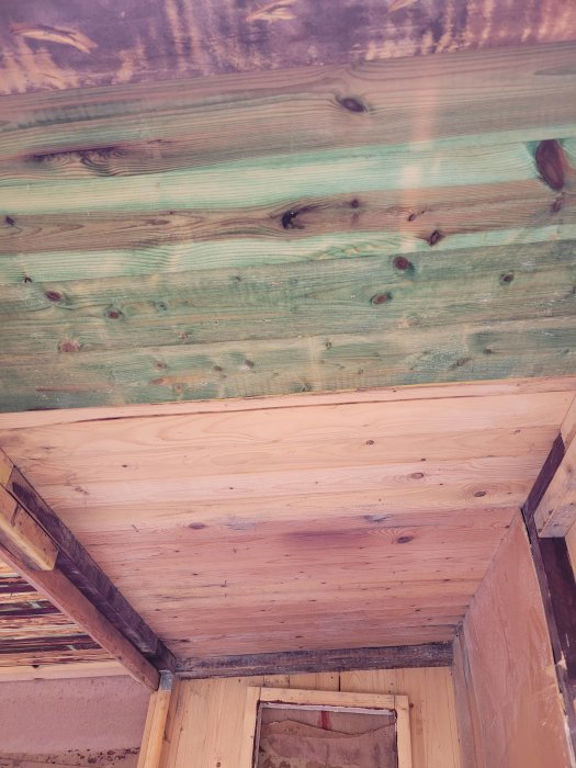 Träpaneler på väggar och tak i ett hörn, synlig träkonstruktion, oavslutad byggnad med öppning i golvet.