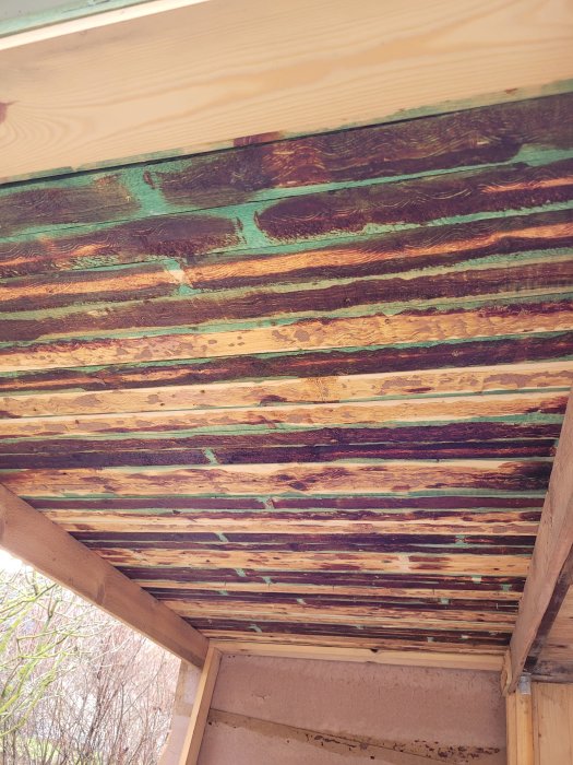 Mångfärgat trä i tak på en utomhuskonstruktion, naturlig textur, rustik känsla, kontrasterande träslag och färgstänk.