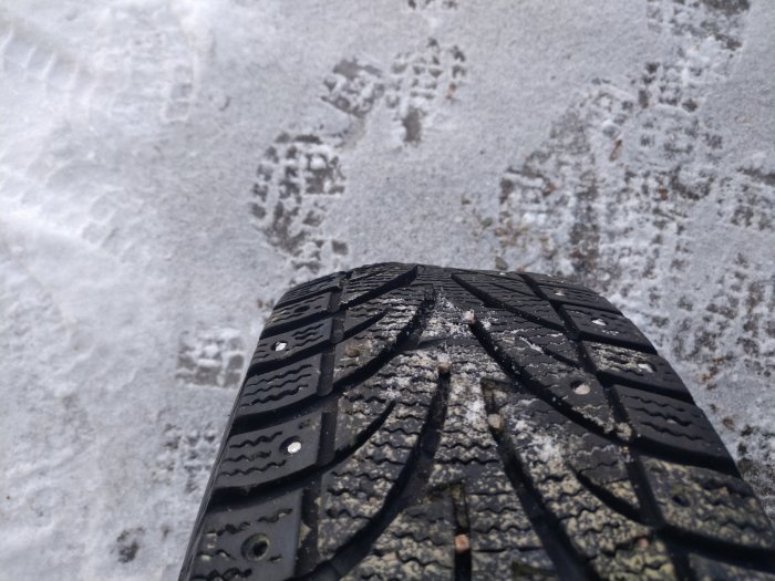 Vinterdäck närbild, mönster, dubbar, asfalt, snötäckt mark med fotspår.