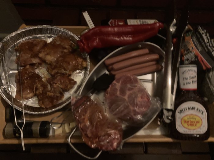 Grilltillbehör: kött, korvar, sås; rött kött i påse, BBQ-flaska; utekvällsförberedelser, grilltema.