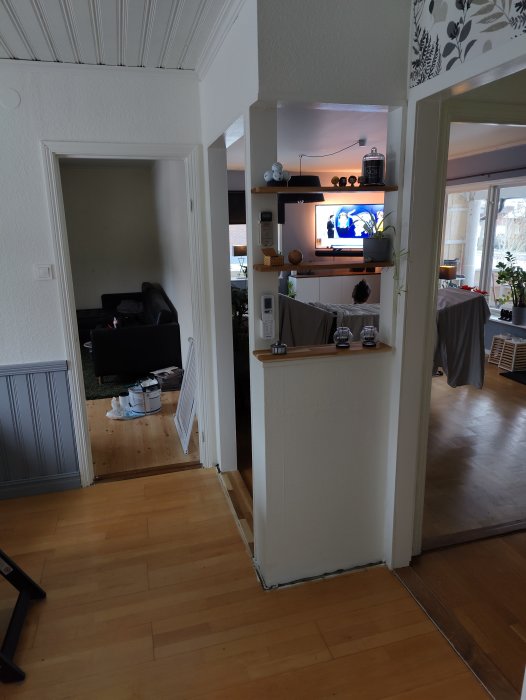 Inuti ett hus med öppen planlösning, trägolv, vit vägg, synligt vardagsrum och TV.