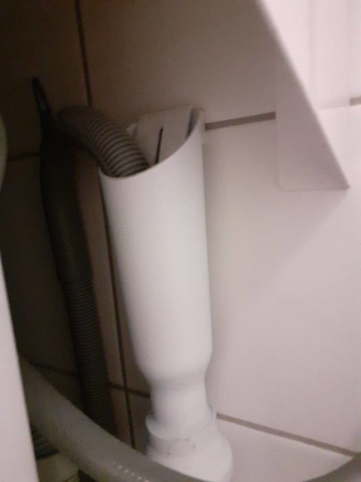 En suddig inomhusbild som visar en upp och nervänd dammsugarslang och tillbehör förvarade i en vit behållare.
