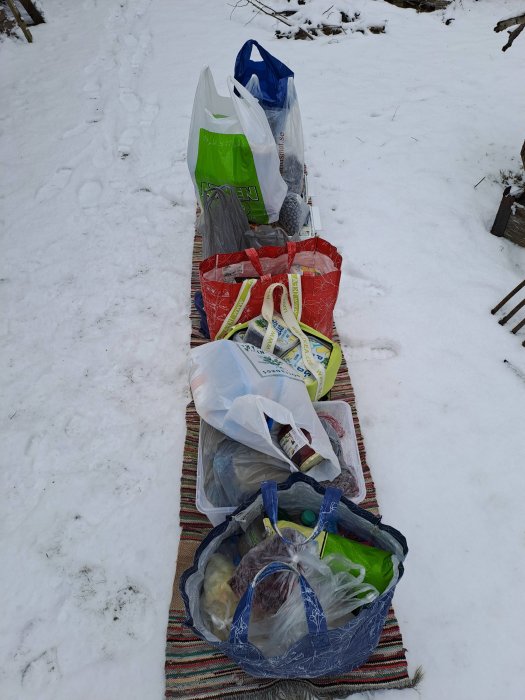 Köpväskor på rad på en matta i snön, spår i bakgrunden, vinterdag, utomhus.