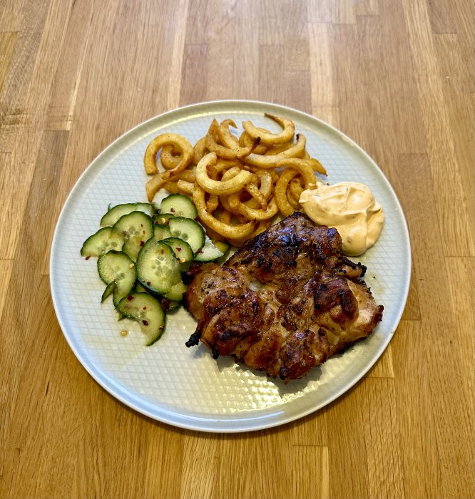 Grillad kyckling, curly fries, gurksallad, chipotlemajonnäs, ljustallrik, träbord.
