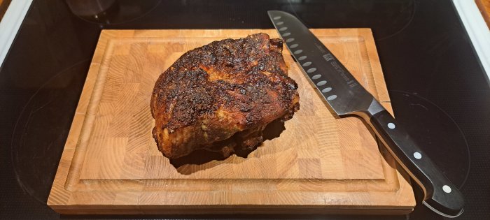 Stekt köttbit på skärbräda bredvid en kökskniv på spis.