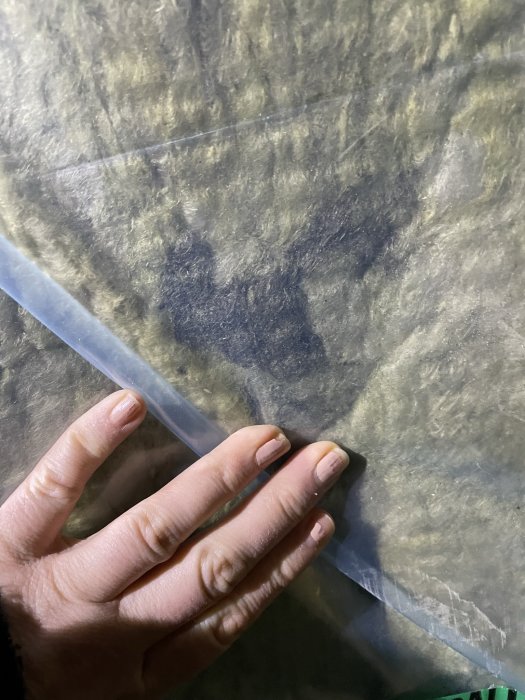 En hand vidrör en genomskinlig plastfilm över en oskarp, texturerad yta. Natt, mystisk atmosfär.