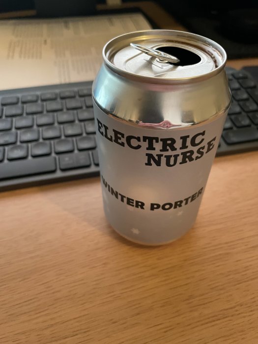 Öppnad dryckesburk märkt "ELECTRIC NURSE WINTER PORTER" framför tangentbord på träbord.