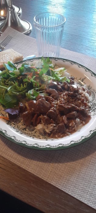 Ett måltid med ris, köttgryta, sallad, bröd och ett glas på bordet.