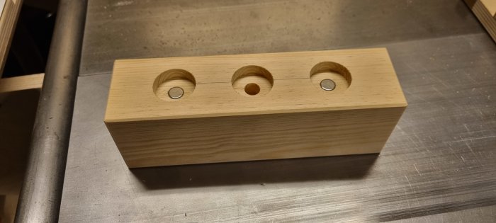 Träblock med tre hål och två metallbrickor på en metallisk yta.