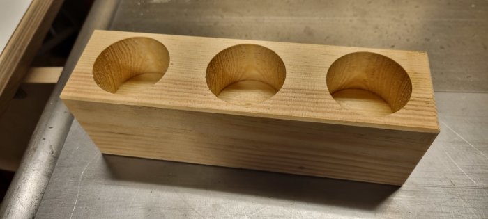 Träblock med tre cirkulära urgröpningar på metallbänk, snickeri eller hantverk, enkel och ren design.