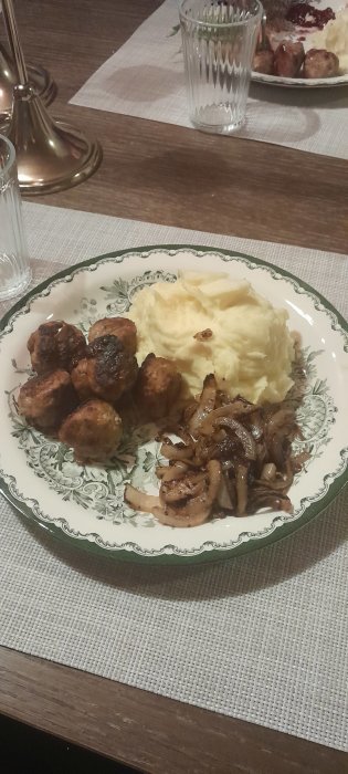 Traditionellt svenskt måltid med köttbullar, potatismos, stekt lök och lingonsylt på dekorativ tallrik.