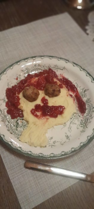 Två köttbullar med potatismos och lingonsylt på dekorativ tallrik, maträtt på bord, silverfärgad sked.