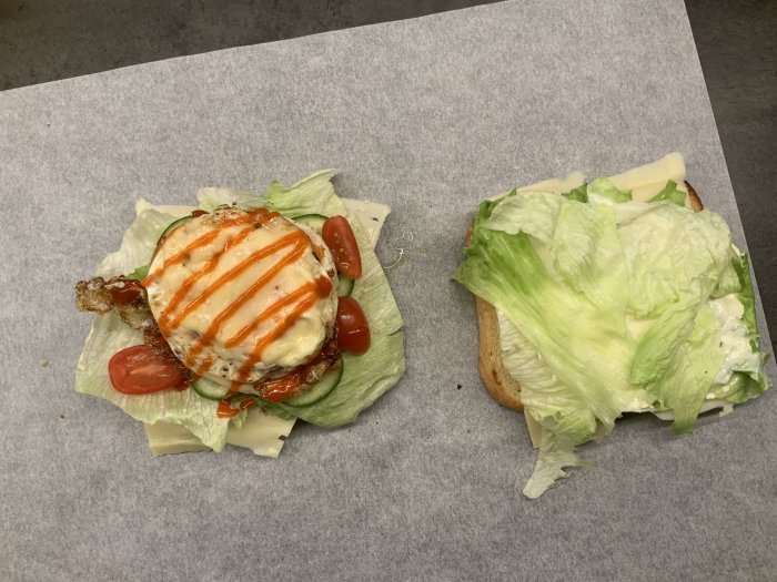 Öppen smörgås med sallad, tomat, ost, dressing och en stekt äggvita på vitt papper.