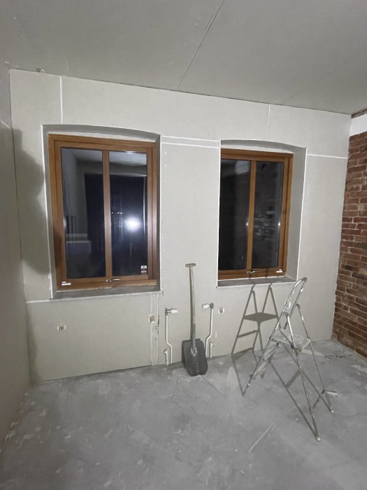 Renoveringsprojekt, ofärdigt rum, två fönster, tegelvägg, gipsskivor, spackel, byggställning, skottkärra, tomma eluttag.