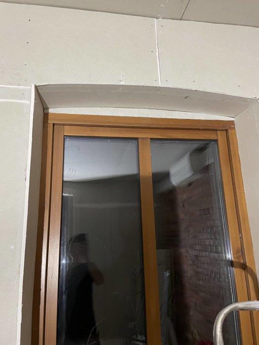 Oavslutat byggarbete kring fönster, gipsskivor, träram, reflexion av person, inomhus, byggmaterial, renovering pågår.