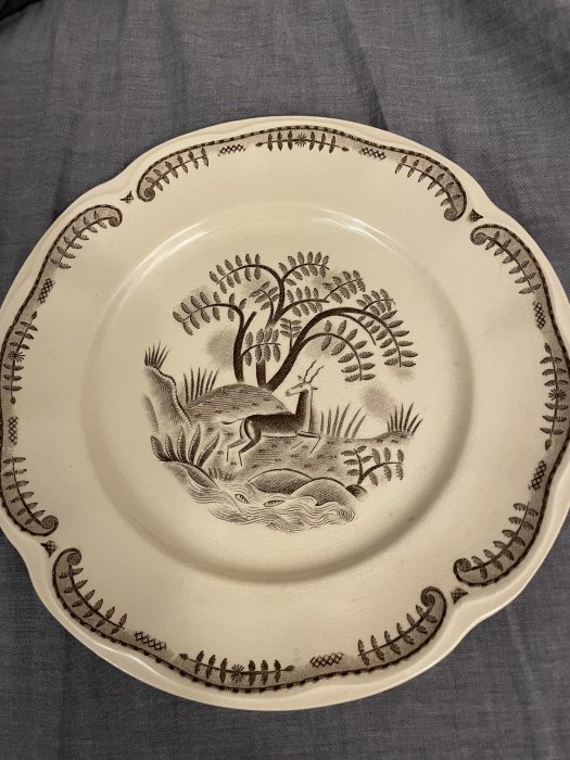 Vitt keramiktallrik med bruna illustrationer av djur och natur, vintagestil, dekorativ kant, traditionellt mönster.