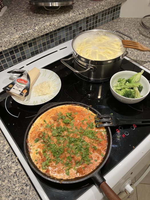 Pasta kokar, omelett med grönsaker steks, broccoli förberedd, riven ost på tallrik, köksmiljö.
