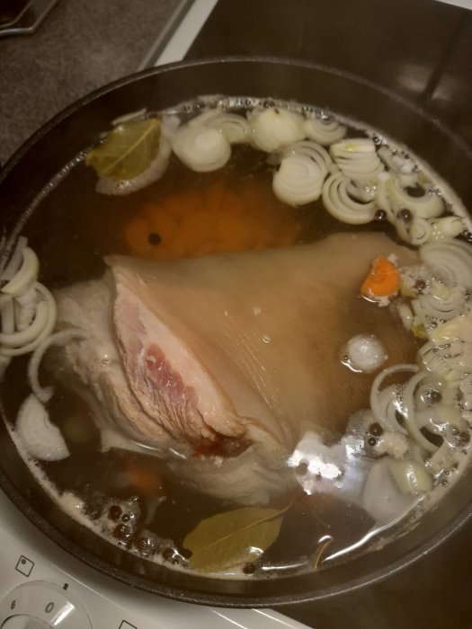 Köttsoppa kokas med lök, morötter, lagerblad och kryddpeppar på spis.