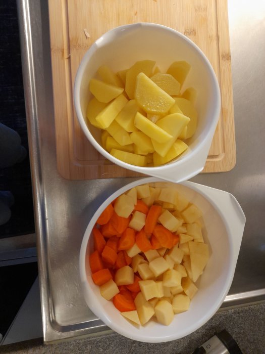 Två skålar med tärnade rotfrukter, morötter och potatis, på köksbänk bredvid skärbräda.