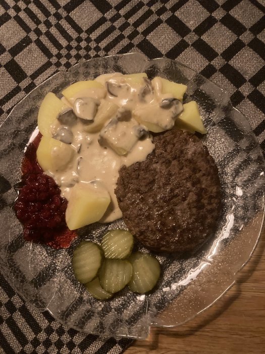 Svensk husmanskost: köttbullar, potatis, gräddsås, lingonsylt och inlagd gurka på rutig duk.