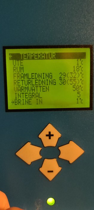 Digital display som visar temperaturvärden, navigeringsknappar nedanför, på en blå vägg.
