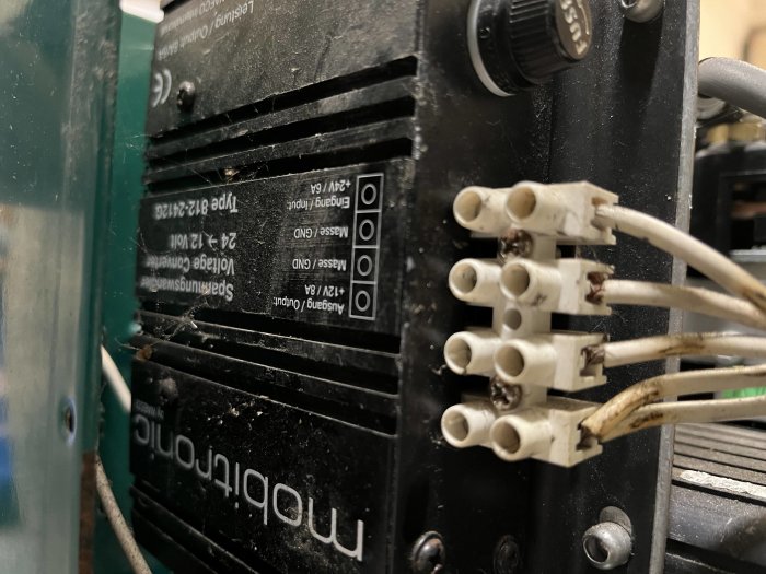 En elektronisk apparat med fläkt, terminalblock och oanslutna trådar. Enheten verkar dammig och något sliten.