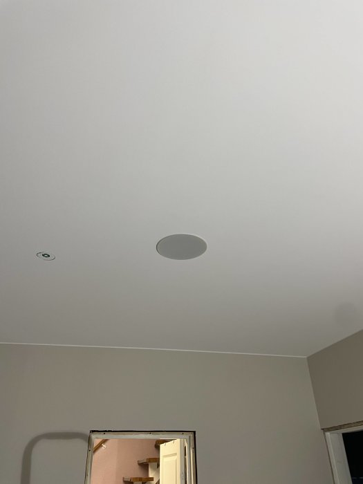 Inomhus vy: tak med infälld spotlights, vit målning, del av trapp och dörröppning.