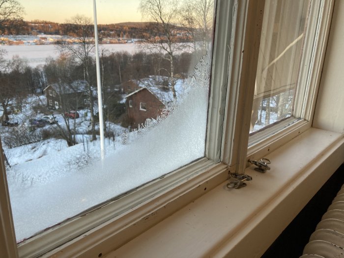 Vy med frost, utsikt över snötäckt landskap och röda hus, vinterdag med solnedgång, lugn och tyst atmosfär.