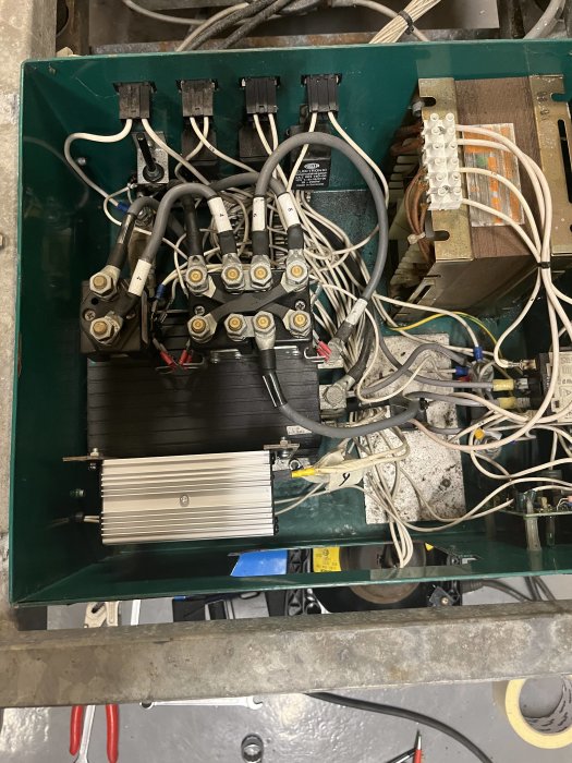 Ett öppet elektriskt styrsystem med sladdar, kontaktorer och en kylfläns inuti en grön metalllåda.