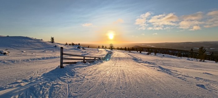 Vinterlandskap vid solnedgång, snötäckta kullar, trädstaket, klara himlen, orörd snö, fridfullt, vidsträckt utsikt.