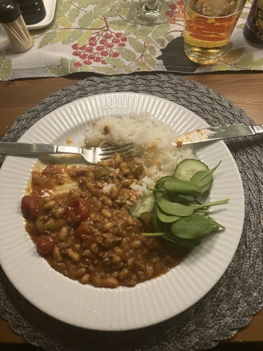 Middagsdukning med tallrik med ris, köttfärssås, bönor, spenat, bestick och ett glas dryck.