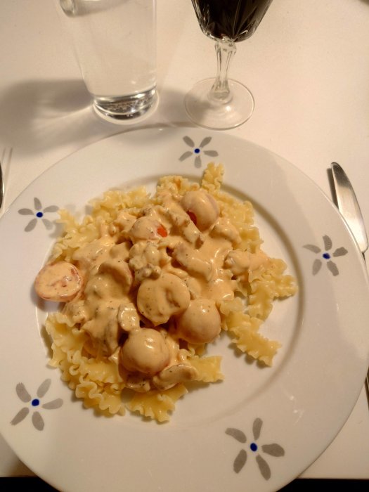 Ett fat med pasta och köttbullar i sås, vattenglas och vinglas, på ett dukat bord.