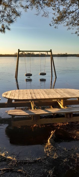 Gungställning i vatten vid solnedgång, brygga i förgrunden, barrträd och stilla vatten. Fridfullt och tyst.