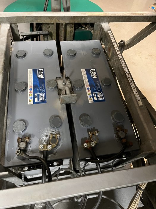Två industriella batterier i metallställning med ledningar och poler synliga, möjligtvis för en maskin eller fordon.