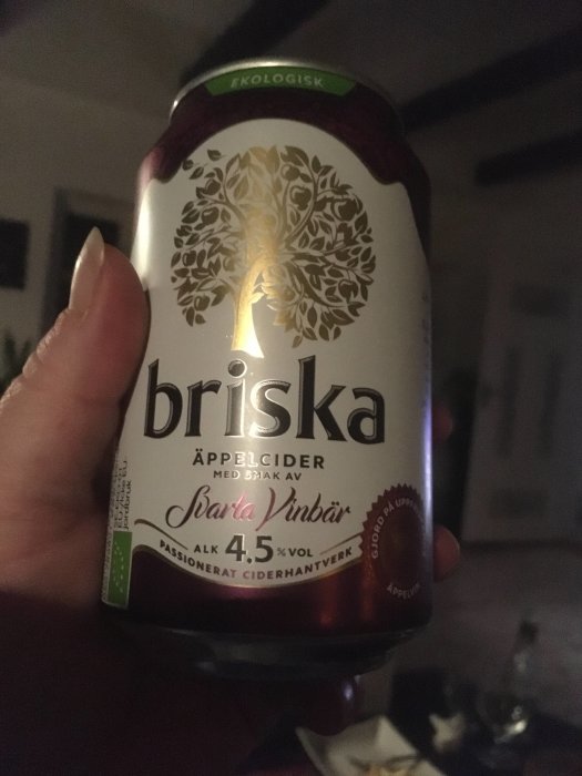 En hand håller en burk ekologisk Briska äppelcider med smak av svarta vinbär.