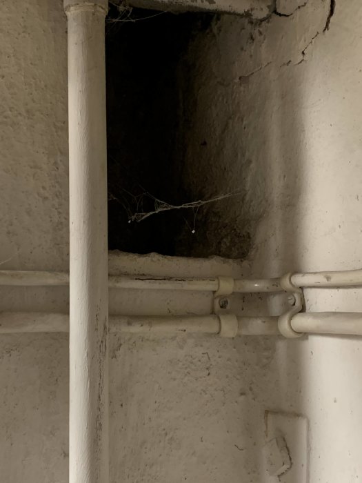 Rörledningar på en sliten vägg, spindelnät, öppning i betongen, strukturerade ytor, gammalt underhållsområde.
