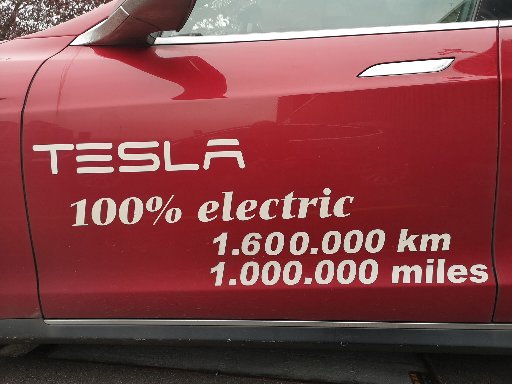 Röd Tesla-bil med text som indikerar att den är helt elektrisk och har kört över en miljon mil.