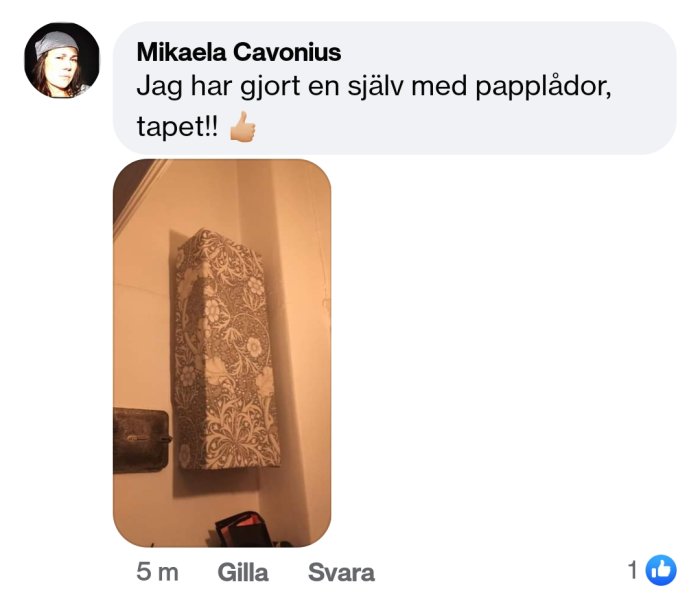 En tavla gjord av pappkartong med mönstrad tapet hänger på en vägg.