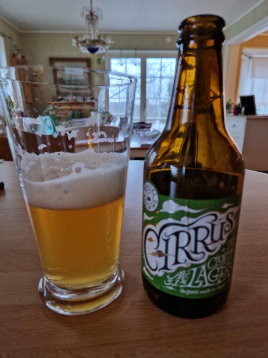 Ett glas med öl och en ölflaska märkt 'Cirrus', inomhus, suddig bakgrund av ett rum.