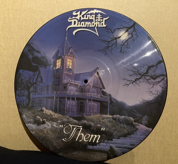 Vinylskiva med spöklikt husmotiv, "King Diamond" bandlogga, albumtiteln "Them" i förgrunden.