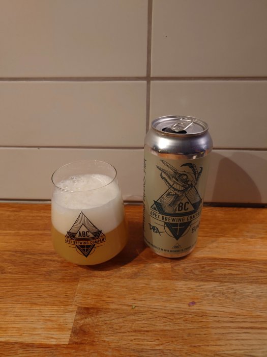 En ölburk och ett glas skummande öl på ett träbord framför kakelvägg.
